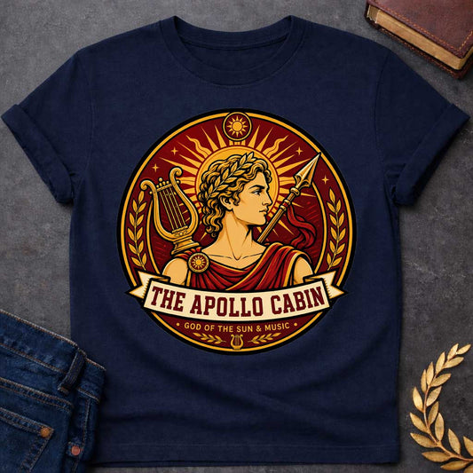 Navy t-shirt with a Apollo Greek mythology cabin design featuring the god of the sun and music wearing a golden laurel crown, framed by a radiant sun, lyre, spear, stars, and laurel branches. Rich red, gold, and cream circular camp-style emblem includes the text “The Apollo Cabin” and “God of the Sun & Music.