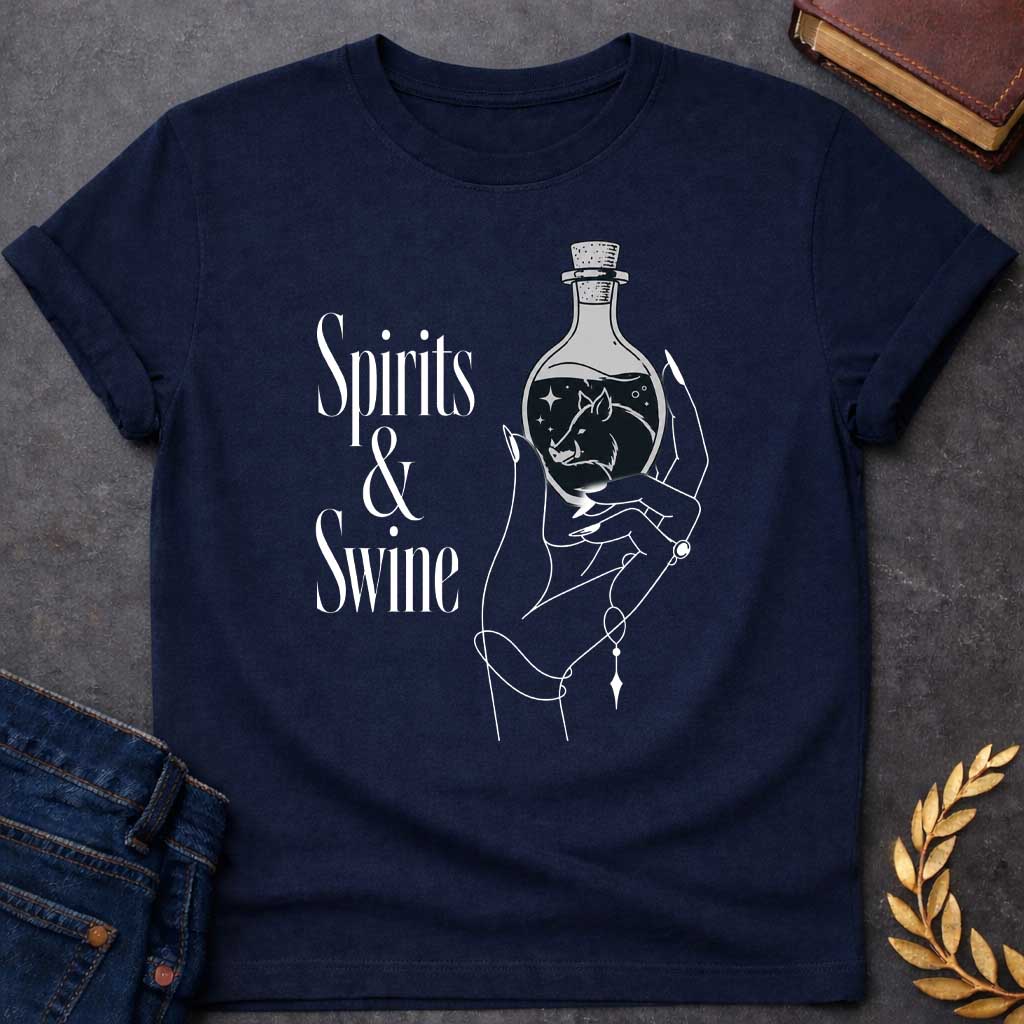 Navy T-shirt with a Minimalist line art illustration of a mystical hand holding a potion bottle labeled 'Spirits & Swine.' Inside the dark bottle, a pig silhouette appears amid glowing stars and magical elements. The elegant hand wears decorative bracelets and rings. Black and white aesthetic with witchy, occult vibes. References Circe's legendary enchanted spirits that transformed men into swine. Celebrates ancient magic, potion-making, and mythological transformation with modern witchcraft themes.