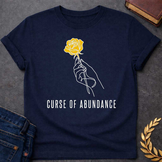Navy t-shirt with A Minimalist Greek mythology design featuring a continuous line-art hand delicately holding a golden rose, symbolizing King Midas' legendary golden touch. Below the illustration, the phrase "Curse of Abundance" appears in clean, modern typography. A simple black-and-gold aesthetic creates an elegant, understated design inspired by the tragic Midas myth.