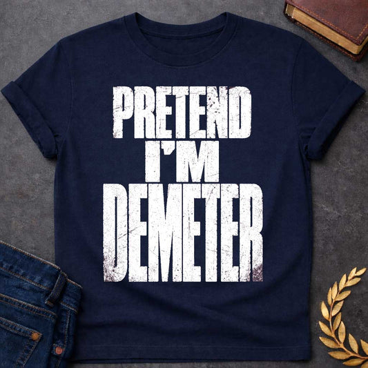 Navy t-shirt with a Pretend I’m Demeter Greek mythology design featuring bold distressed white typography on a transparent background. The stacked text reads “PRETEND I’M DEMETER” in a rugged vintage block font, creating a humorous design inspired by Demeter, the Greek goddess of agriculture, harvest, grain, fertility, and the earth.