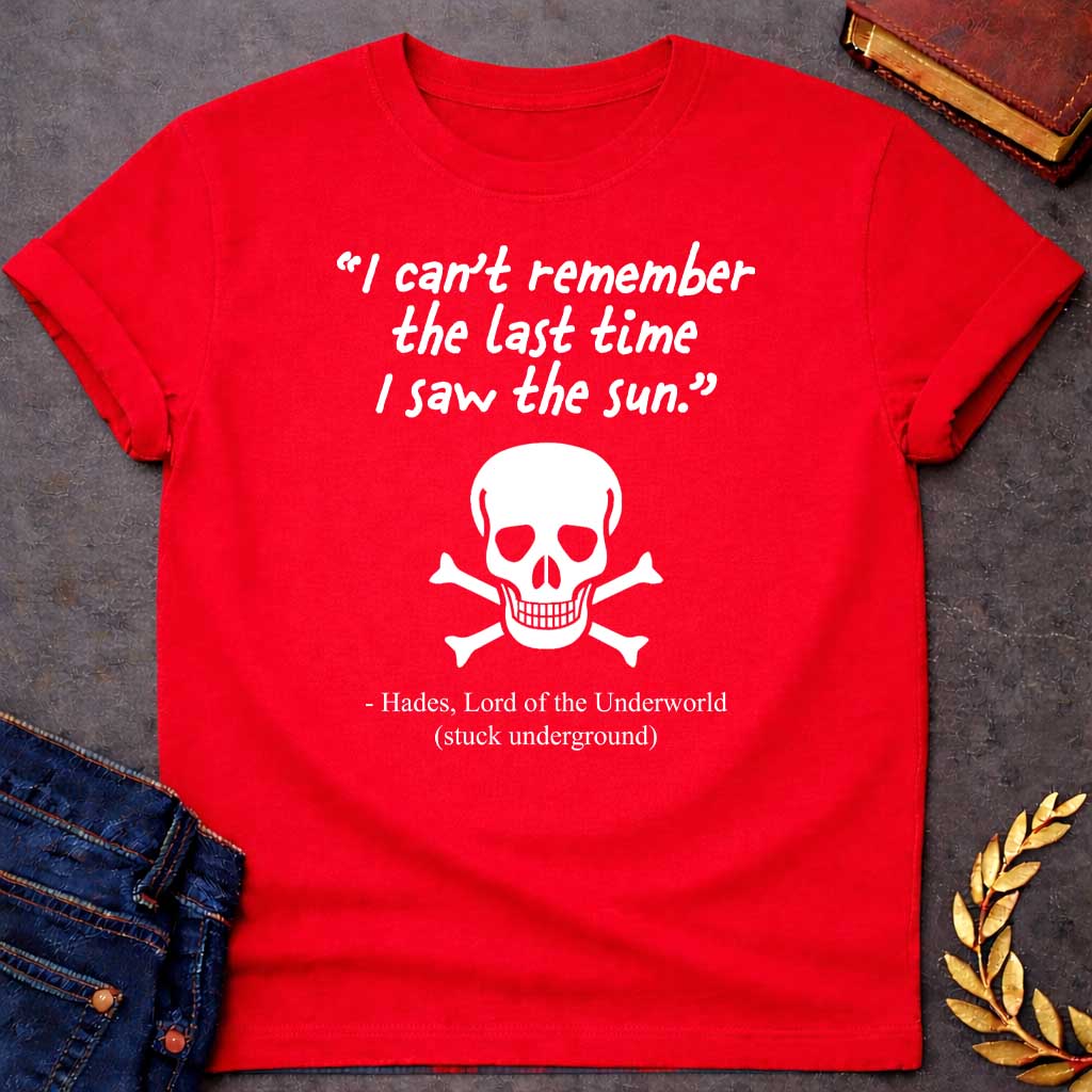 Red T-shirt graphic in black and white featuring a handwritten-style quote reading "I can't remember the last time I saw the sun." above a classic skull and crossbones illustration, with the humorous attribution below reading "- Hades, Lord of the Underworld (stuck underground)
