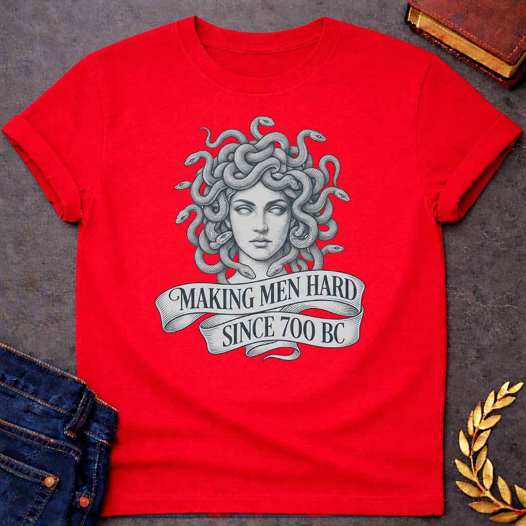 Red T-shirt graphic in grey and white featuring a highly detailed fine-line tattoo-style front-facing portrait of Medusa with numerous coiling snakes for hair, rendered in intricate stippling and engraving technique, with a flowing ribbon banner below reading "Making Men Hard Since 700 BC" — a witty double entendre referencing Medusa's mythological power to turn men to stone