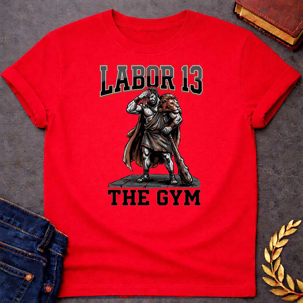 Red T-shirt featuring a sweat-drenched, muscular figure resembling Heracles, wearing a lion-skin cloak and holding a large wooden club. He stands on a stone platform while wiping his brow with a towel. The text "LABOR 13" is printed in large, bold, block letters across the top, and "THE GYM" is in a matching style at the bottom