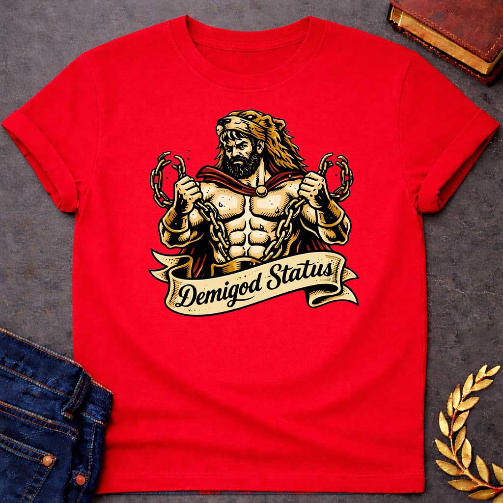 Red T-shirt featuring a muscular, bearded figure resembling Heracles, wearing a lion-skin hood and a red cape, as he heroically snaps thick golden chains with his hands. Below the illustration is a flowing, decorative banner with the text "Demigod Status" written in a stylish script font,