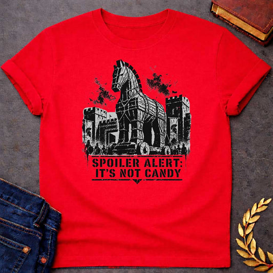 Red T-shirt with a graphic in black featuring a gritty detailed ink splatter-style illustration of the Trojan Horse towering over the walls of Troy, flanked by Spartan warriors with shields and spears and castle battlements with birds circling overhead. Bold military stencil text in a distressed banner below reads "Spoiler Alert: It's Not Candy" — a humorous reference to the Greek legend of the Trojan War