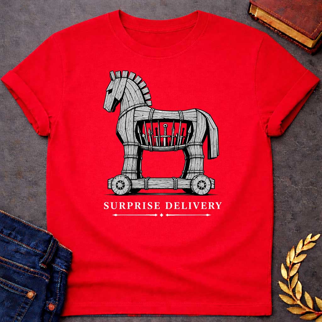 Red T-shirt with a graphic in black and white featuring a highly detailed realistic ink illustration of the Trojan Horse constructed from weathered wood planks bound with rope on a wheeled platform, with spears and a sword visibly hidden inside its hollow body. Elegant spaced serif text below with decorative arrow dividers reads "Surprise Delivery" — a humorous reference to the Greek legend of the Trojan War