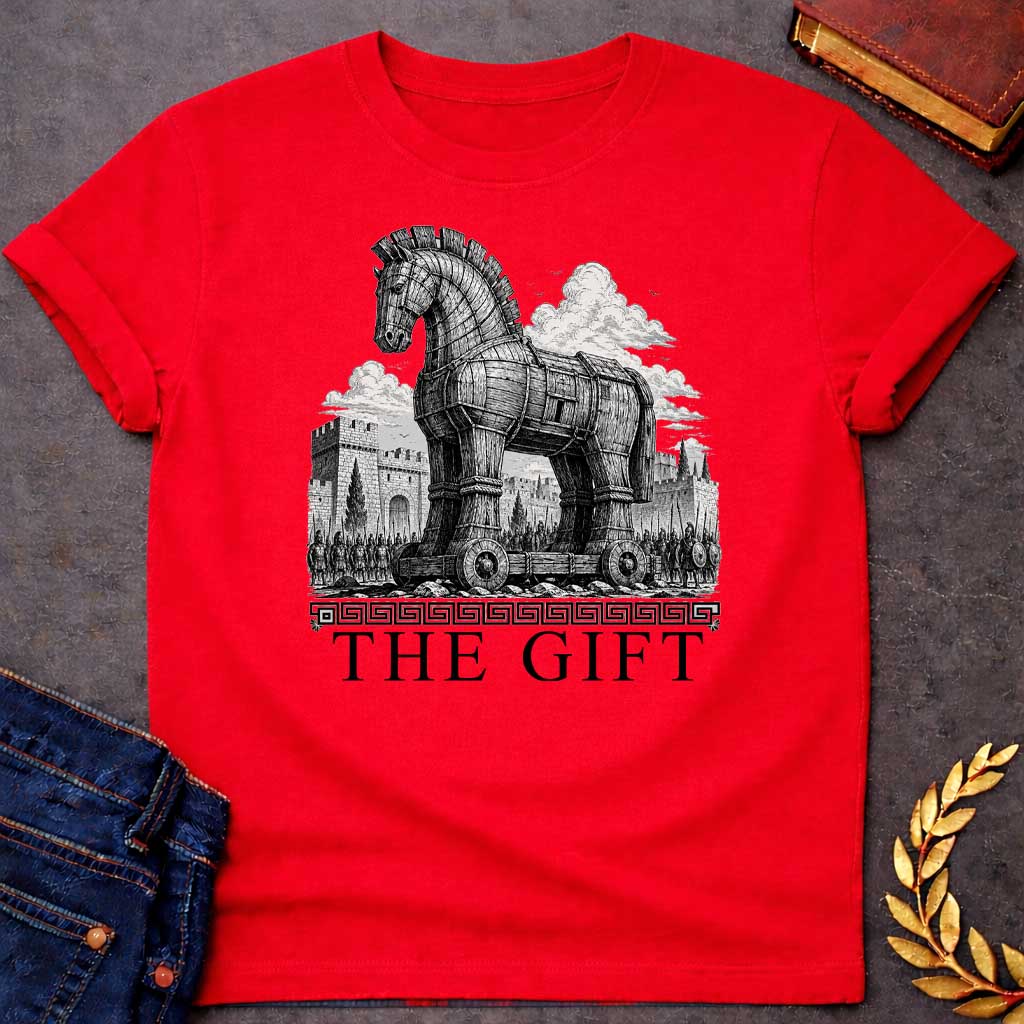 Red T-shirt with a graphic in black featuring an exceptionally detailed fine-line engraving-style illustration of the Trojan Horse towering over the walls of Troy, surrounded by crowds of armored Greek soldiers with spears and shields, set against dramatic billowing clouds. A Greek meander border separates the scene from large bold classical serif text below reading "The Gift" — an ironic reference to the Greek legend of the Trojan War