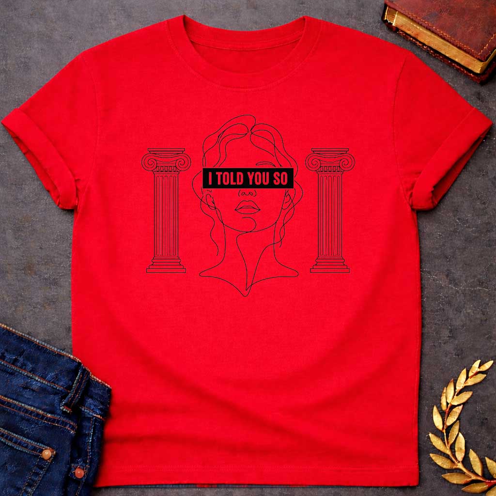 Red T-shirt with a minimalist line art design featuring a continuous black ink sketch of Cassandra or a Greek goddess. Her eyes are covered by a bold, solid black rectangular bar with the text "I TOLD YOU SO" in white sans-serif capital letters. The portrait is flanked on both sides by simple, symmetrical line-drawn Ionic Greek columns.