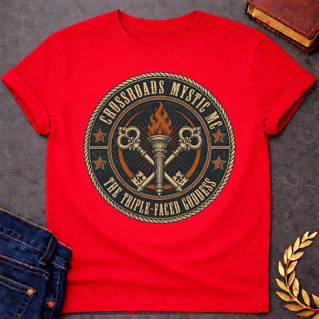 Red T-shirt with a Motorcycle club patch-style emblem in navy, gold, and orange inspired by Hecate and crossroads mythology. A central ornate torch with orange flames is flanked by two crossed serpent handles with decorative gold scrollwork. Radiating lines suggest divine power. Text reads 'Crossroads Mystic MC' and 'The Triple-Faced Goddess' around the border. Orange stars and rope border complete the official club patch look. Distressed texture adds authentic biker aesthetic.