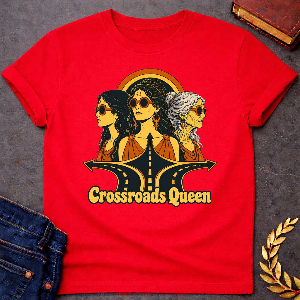 Red T-shirt with a Glamorous retro illustration of Hecate as 'Crossroads Queen' in gold and orange with 70s aesthetic. Three female faces wear oversized round sunglasses and gold jewelry including crescent moon symbols and hoops. Center figure wears a crescent moon bindi. All wear draped orange clothing. A golden halo radiates behind them. Below, stylized black roads with yellow center lines converge at a crossroads. Text reads 'Crossroads Queen' in gold.