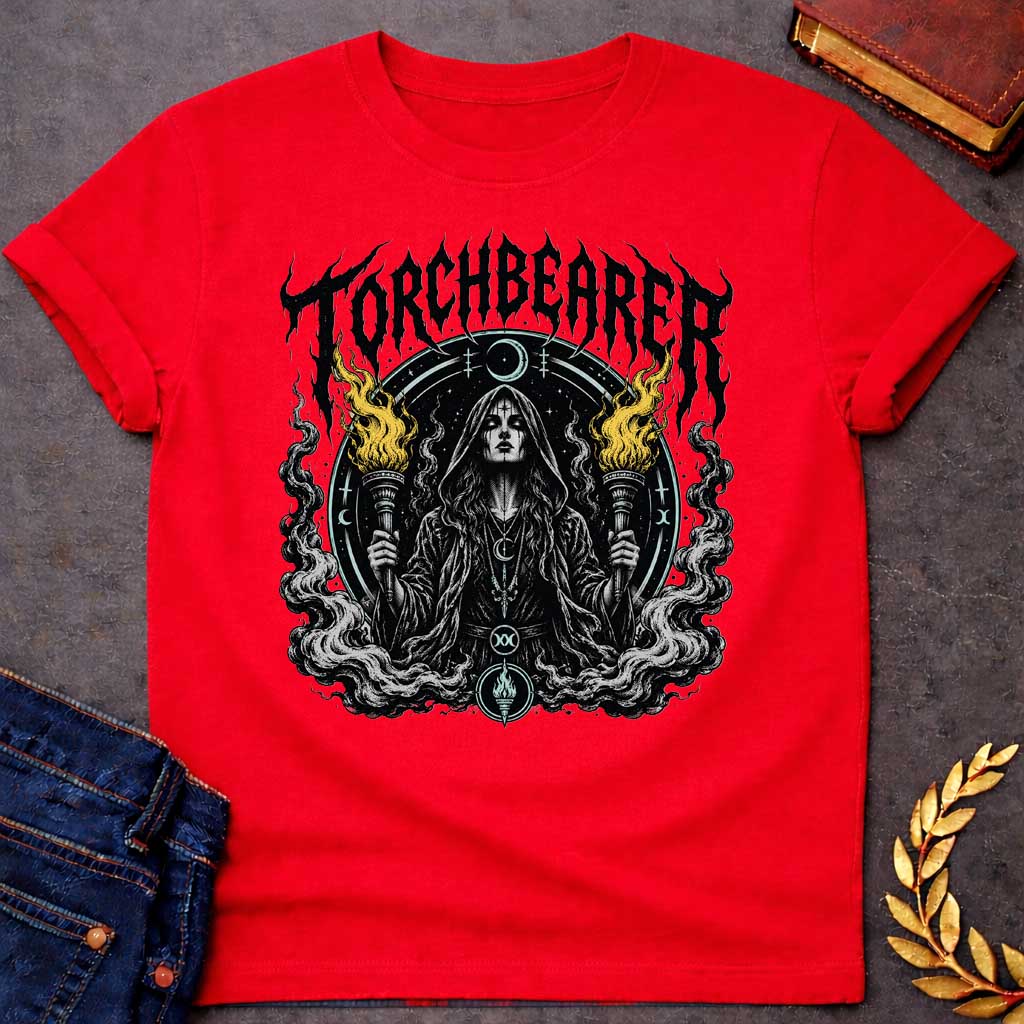 Red T-shirt with a Dark metal band aesthetic illustration titled 'Torchbearer.' Hecate holds two ornate torches with gold and black flames. She wears mystical symbols including a crescent moon necklace and a circular mandala halo with occult iconography. Swirling smoke and flame designs surround the figure in black, white, and gold. Blends heavy metal imagery with Greek mythology and mystical symbolism celebrating enlightenment, divine knowledge, and dark power.