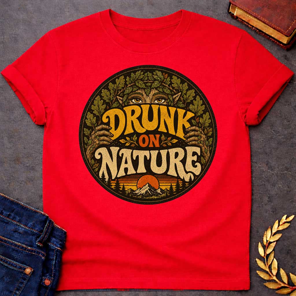 Red T-shirt with a vintage, retro-style t-shirt graphic enclosed in a circular badge. At the top, the intense gold eyes of a forest nymph or dryad peek out from behind a thick crown of oak leaves. Earthy, stylized 1970s block text proudly reads "DRUNK ON NATURE" in gold and cream. The bottom of the design showcases a serene mountain landscape and a setting sun, framed by rustic pine trees and a distressed texture