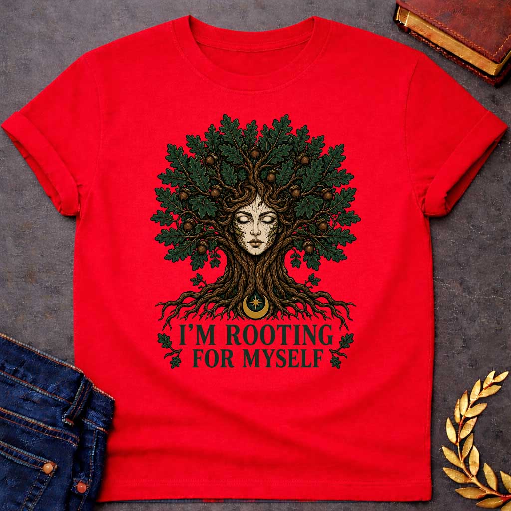 Red T-shirt with a cottagecore-style graphic featuring a detailed illustration of an oak tree dryad or nature spirit. Her serene, closed-eyed face forms the center of the tree trunk, with gnarled roots expanding below and a massive canopy of dark green oak leaves and brown acorns spreading above. Underneath the roots, a pun-based tagline reads "I'M ROOTING FOR MYSELF" in a bold, clean green serif font.