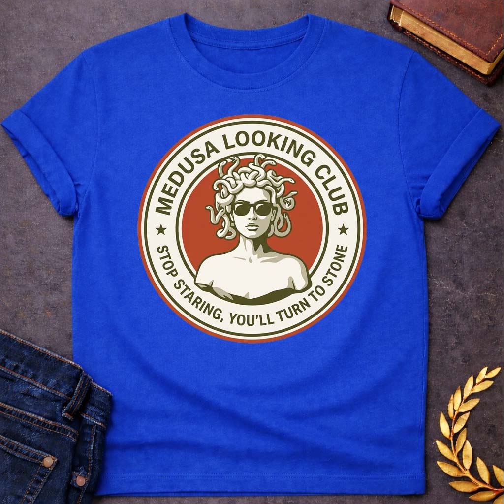 Royal Blue t-shirt in retro badge style: a cool, sunglasses-wearing Medusa with snake hair stands confidently against a burnt-orange circle. Cream and olive-green ring text reads "Medusa Looking Club" above and "Stop Staring, You'll Turn to Stone" below, with two stars flanking the design.