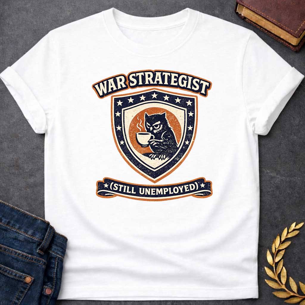 White T-shirt graphic featuring a vintage varsity-style crest in navy, orange, and cream. A grumpy owl holding a steaming coffee cup is centered on a shield surrounded by stars. An arched banner above reads "War Strategist" and a ribbon banner below reads "(Still Unemployed)," giving the design a humorous tone