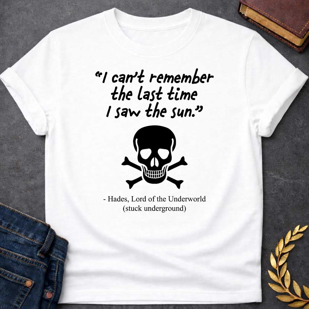 White T-shirt graphic in black and white featuring a handwritten-style quote reading "I can't remember the last time I saw the sun." above a classic skull and crossbones illustration, with the humorous attribution below reading "- Hades, Lord of the Underworld (stuck underground)