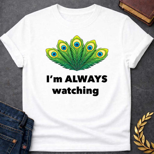 White T-shirt graphic featuring a vibrant illustrated fan of five peacock feathers in rich green, yellow, and blue tones, each with a distinctive eye-spot, above text reading "I'm Always Watching" — a humorous reference to Hera, the Greek Queen of the Gods, whose sacred symbol is the peacock