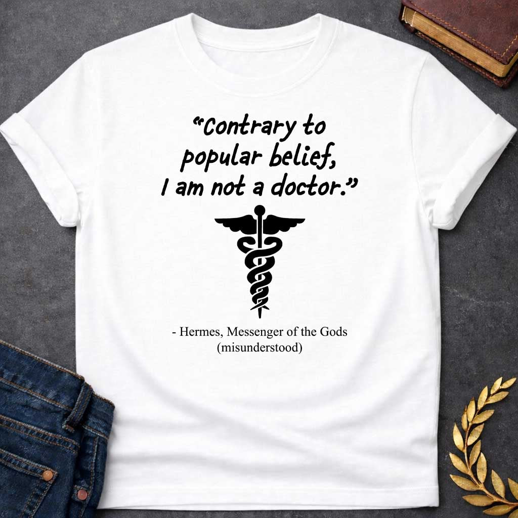 White T-shirt graphic in black text featuring a handwritten-style quote reading "Contrary to popular belief, I am not a doctor." above a black caduceus symbol, with the humorous attribution below in serif text reading "- Hermes, Messenger of the Gods (misunderstood)," playing on the common confusion between Hermes' caduceus and the medical symbol