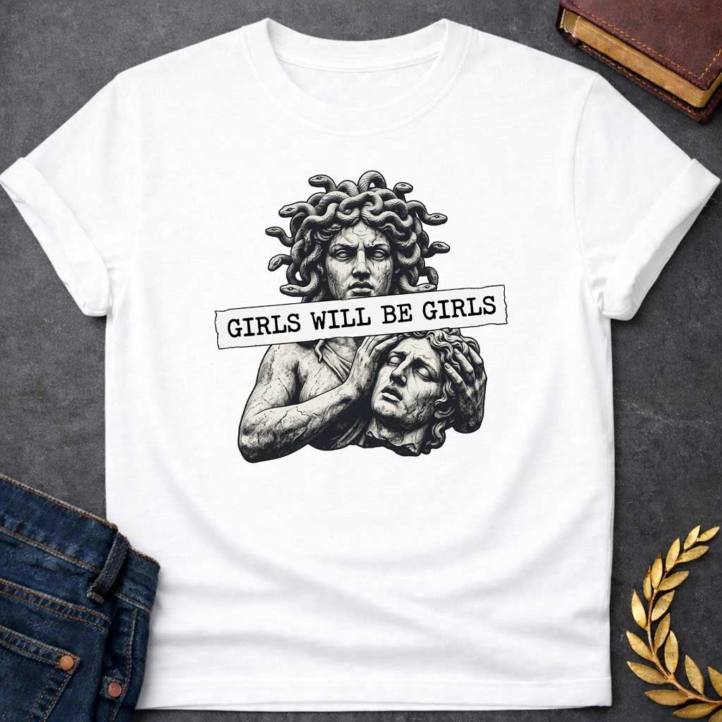White T-shirt graphic in black and white featuring a detailed stone sculpture-style illustration of Medusa with snake hair looming above a distressed male figure clutching his head in anguish, with a torn paper banner across the middle reading "Girls Will Be Girls" in bold typewriter font — a humorous feminist nod to the Greek mythology story of Medusa