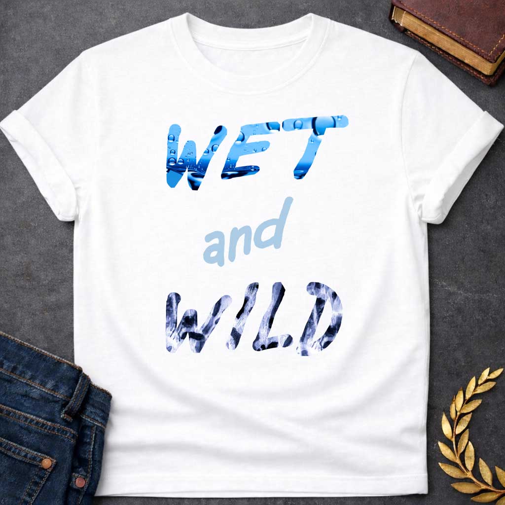 White T-Shirt with a graphic design featuring the phrase "WET and WILD" in three stacked rows. The word "WET" is at the top in a large, bold, sans-serif font. The letters are filled with a high-definition image of bright blue water and splashing droplets. The word "and" is in the center in a smaller, lowercase, light-blue cursive-style font. The word "WILD" is at the bottom in the same large, bold font as "WET," but the letters are filled with a black-and-white leopard or cheetah print pattern