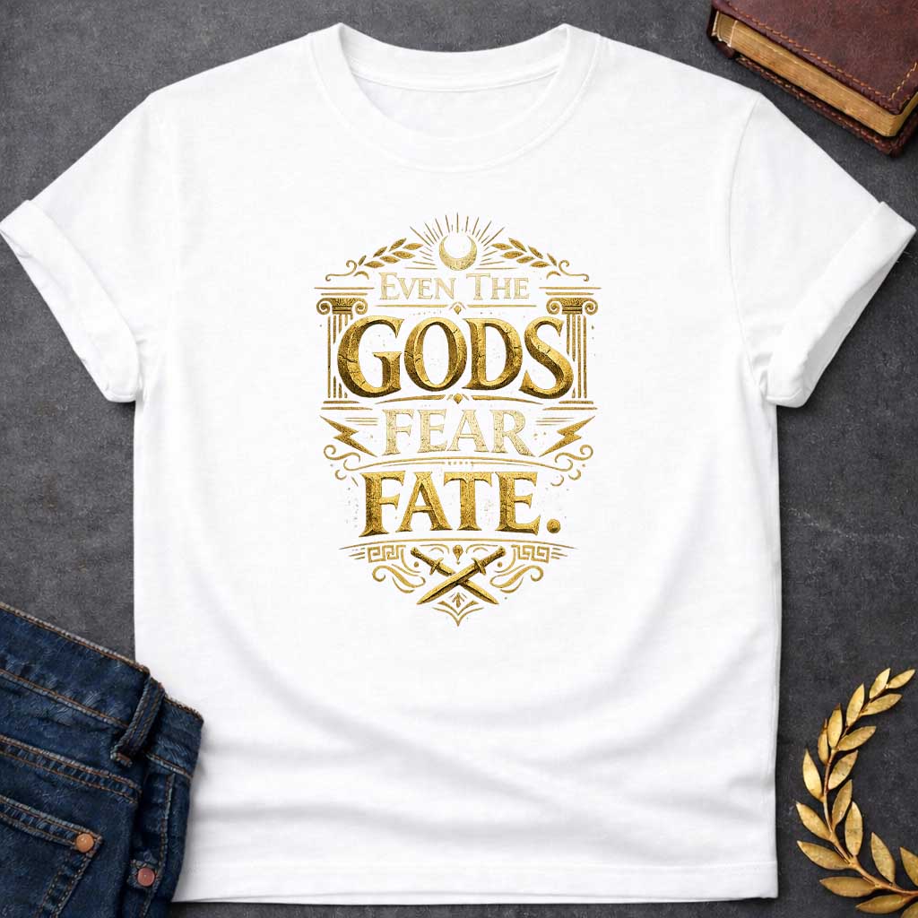 White t-shirt featuring a high-contrast, mythic gold design. The text reads 'EVEN THE GODS FEAR FATE.' in distressed, 3D chiseled gold letters. The typography is framed by Greek architectural elements: an Ionic column on each side, a top crescent moon with laurel branches, jagged lightning bolts, and a bottom section with crossed ancient daggers above a Greek key pattern. The overall aesthetic resembles weathered, metallic ancient stone carvings, creating a vintage and powerful look.