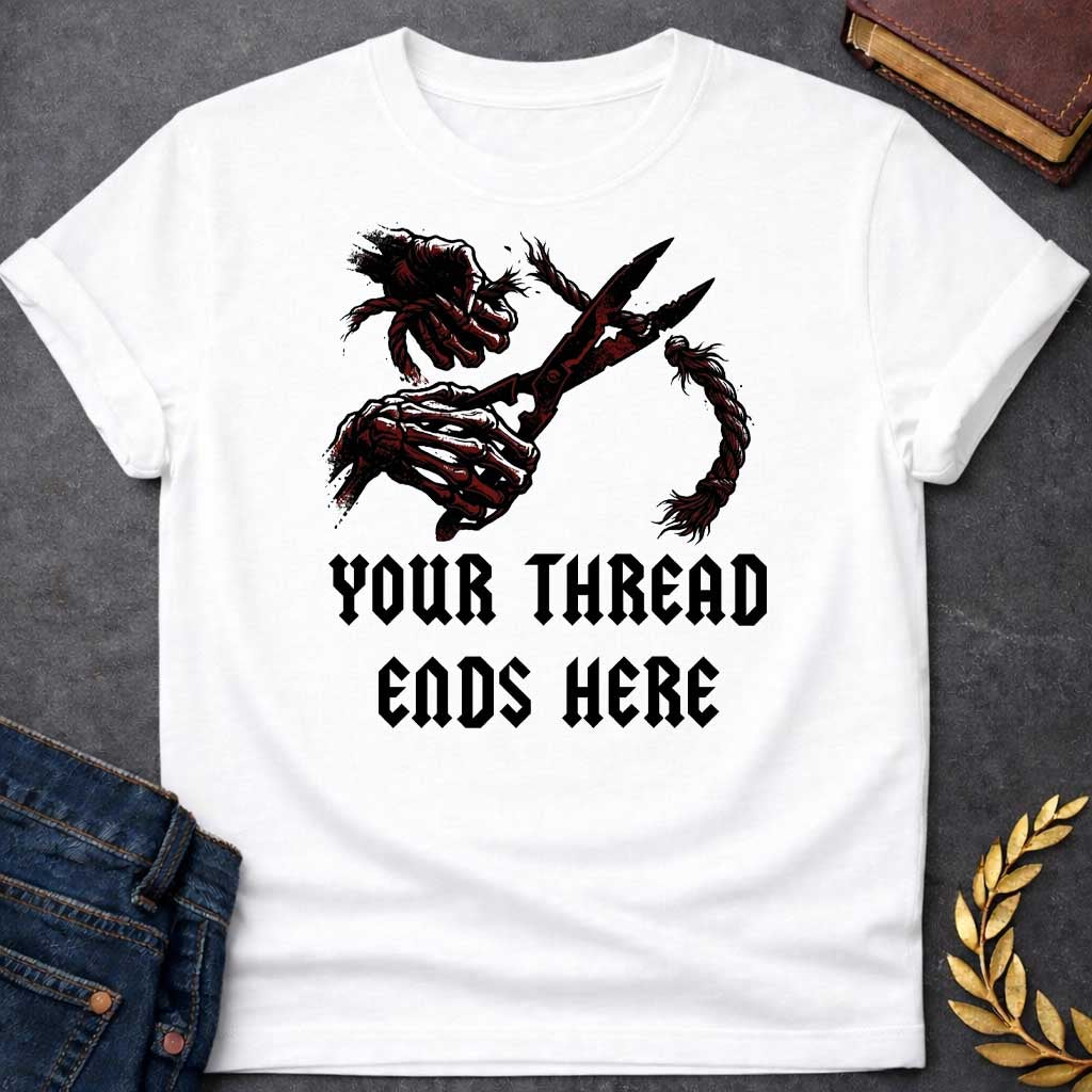 White T-shirt graphic in black, white, and dark red featuring a dark illustrated scene of two skeletal hands gripping large shears cutting through a thick fraying rope or thread, rendered in a gritty horror-influenced ink style with ink splatter details. Bold heavy metal-style blackletter text below reads "Your Thread Ends Here" — a dark and dramatic reference to Atropos, the eldest of the Moirai, the Greek Fate who cuts the thread of life