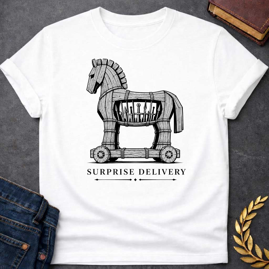 White T-shirt with a graphic in black and white featuring a highly detailed realistic ink illustration of the Trojan Horse constructed from weathered wood planks bound with rope on a wheeled platform, with spears and a sword visibly hidden inside its hollow body. Elegant spaced serif text below with decorative arrow dividers reads "Surprise Delivery" — a humorous reference to the Greek legend of the Trojan War