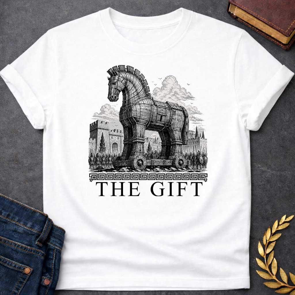 White T-shirt with a graphic in black featuring an exceptionally detailed fine-line engraving-style illustration of the Trojan Horse towering over the walls of Troy, surrounded by crowds of armored Greek soldiers with spears and shields, set against dramatic billowing clouds. A Greek meander border separates the scene from large bold classical serif text below reading "The Gift" — an ironic reference to the Greek legend of the Trojan War