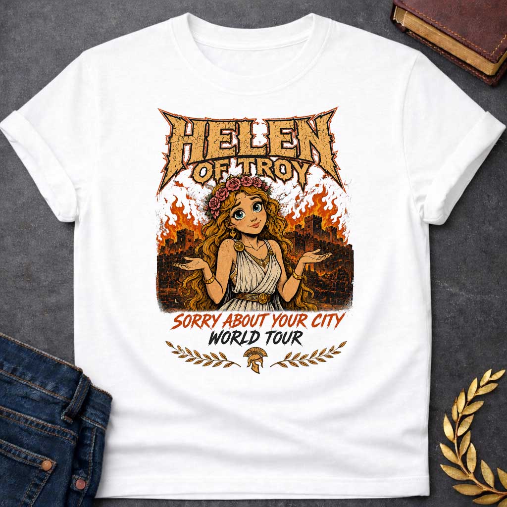 White T-shirt with a heavy metal style graphic featuring a cartoon Helen of Troy with big blue eyes and a flower crown. She shrugs playfully while standing in front of a burning ancient city wall. At the top, "HELEN OF TROY" is written in a jagged, metallic font. Below her, the text reads "SORRY ABOUT YOUR CITY" in orange and "WORLD TOUR" in black brush script, accented by a Spartan helmet and laurel leaves.