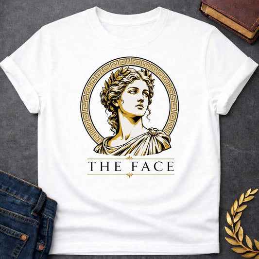 White T-shirt with a classical Greek graphic featuring a gold and cream vector portrait of Helen of Troy in profile. She wears a golden laurel wreath and a traditional draped chiton, looking upward with a serene expression. The portrait is framed by a circular border with a gold Greek key (meander) pattern. Below the emblem, the text "THE FACE" is written in a clean, elegant black serif font between horizontal gold accent lines.