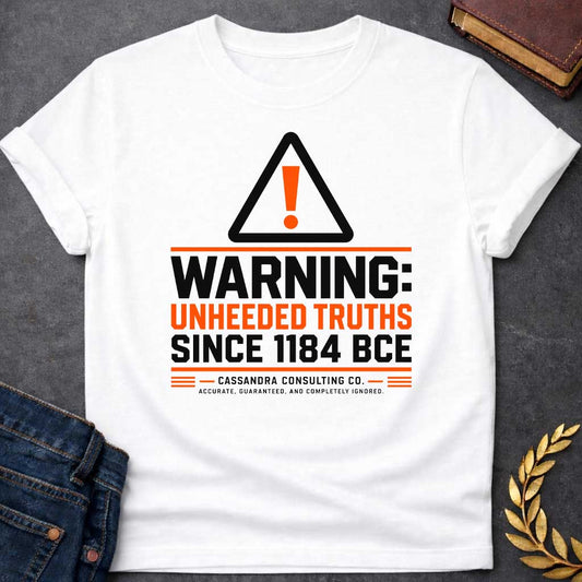 White T-shirt with a corporate-style satirical design mimicking an industrial hazard sign. At the top is a triangular warning icon with an orange exclamation point. Bold block text reads "WARNING: UNHEEDED TRUTHS SINCE 1184 BCE" in alternating black and orange. Below, it features a faux company name: "CASSANDRA CONSULTING CO." followed by the tagline, "ACCURATE, GUARANTEED, AND COMPLETELY IGNORED."