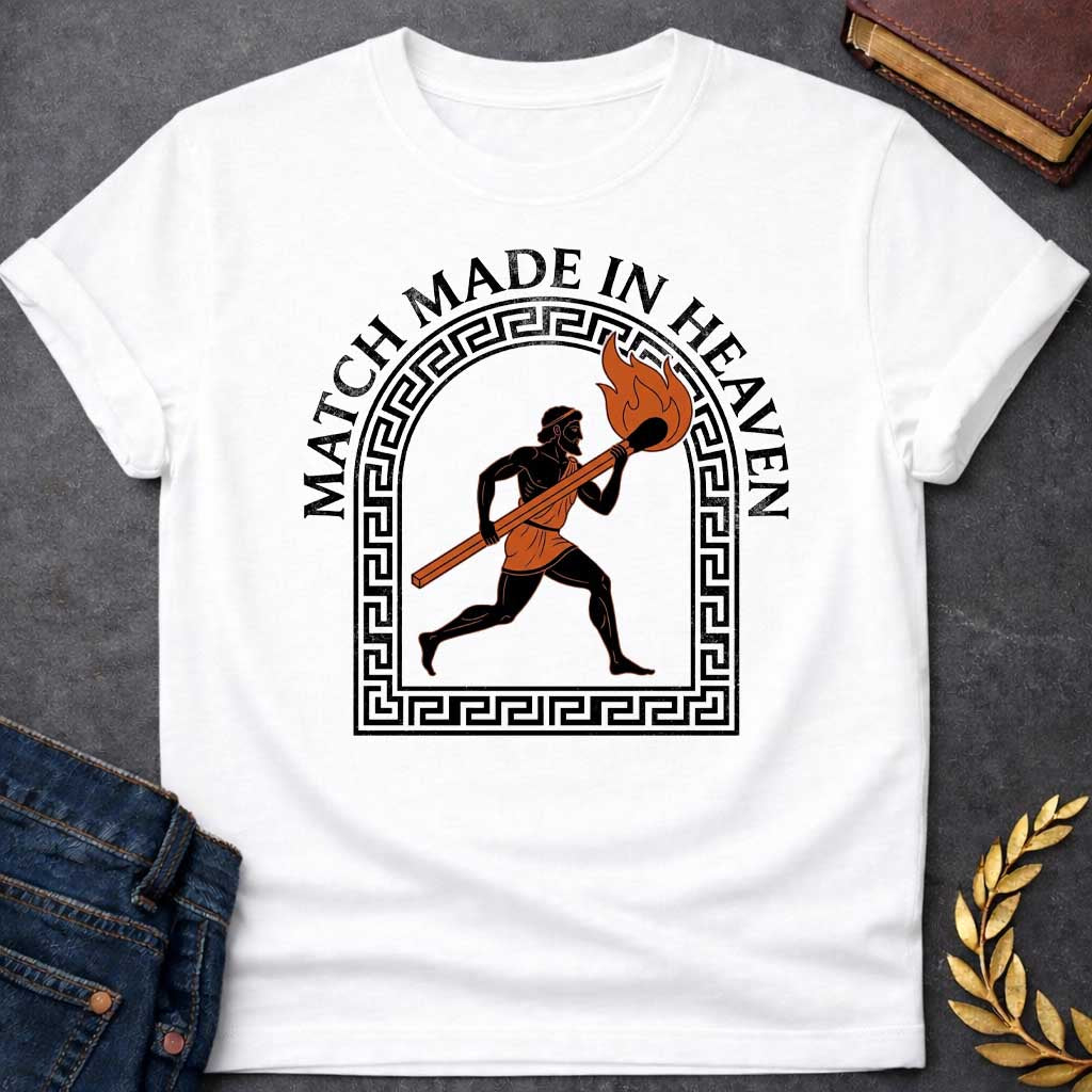 White T-shirt with A graphic in an ancient Greek Black-Figure pottery style featuring Prometheus running while carrying a massive, burning match stick. He is depicted in black silhouette with terracotta-orange details on his tunic and the flame. The figure is framed by a black Greek key meander arch. Above the design, the pun "MATCH MADE IN HEAVEN" is written in an arched, bold black serif font.
