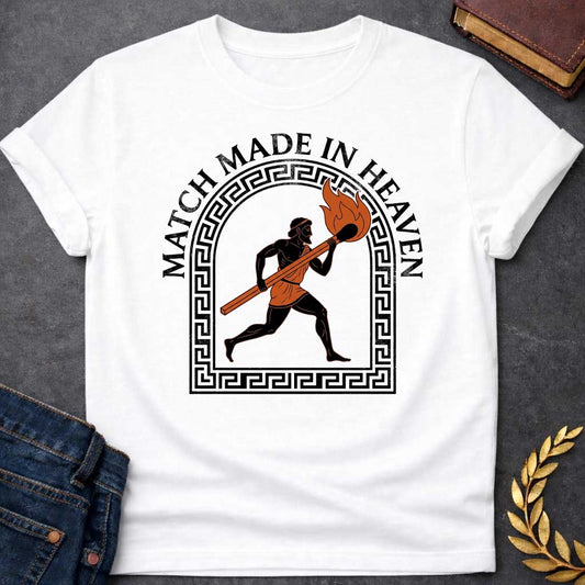 White T-shirt with A graphic in an ancient Greek Black-Figure pottery style featuring Prometheus running while carrying a massive, burning match stick. He is depicted in black silhouette with terracotta-orange details on his tunic and the flame. The figure is framed by a black Greek key meander arch. Above the design, the pun "MATCH MADE IN HEAVEN" is written in an arched, bold black serif font.