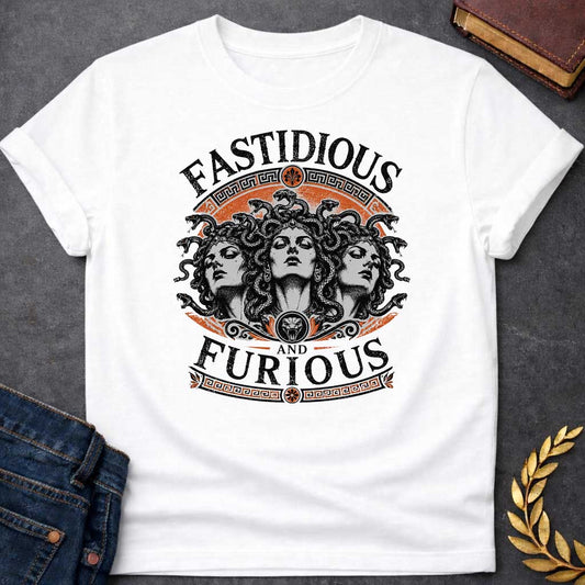 White T-shirt with a Humorous design combining 'Fast and Furious' with Greek mythology. Text reads 'FASTIDIOUS AND FURIOUS' in distressed lettering surrounding three faces of Medusa in black and white engraving style. Detailed serpents with individual scales form her hair. Greek key pattern borders in orange frame the composition with decorative sun motifs and a small snake head icon at center. Blends classical mythology with contemporary pop culture humor and clever wordplay.