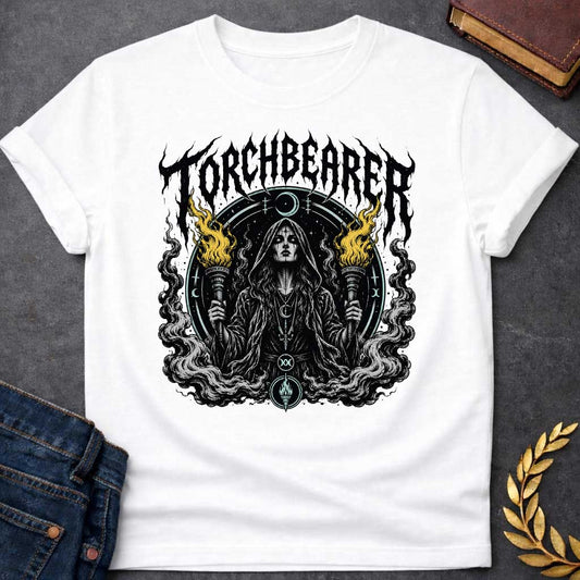 White T-shirt with a Dark metal band aesthetic illustration titled 'Torchbearer.' Hecate holds two ornate torches with gold and black flames. She wears mystical symbols including a crescent moon necklace and a circular mandala halo with occult iconography. Swirling smoke and flame designs surround the figure in black, white, and gold. Blends heavy metal imagery with Greek mythology and mystical symbolism celebrating enlightenment, divine knowledge, and dark power.