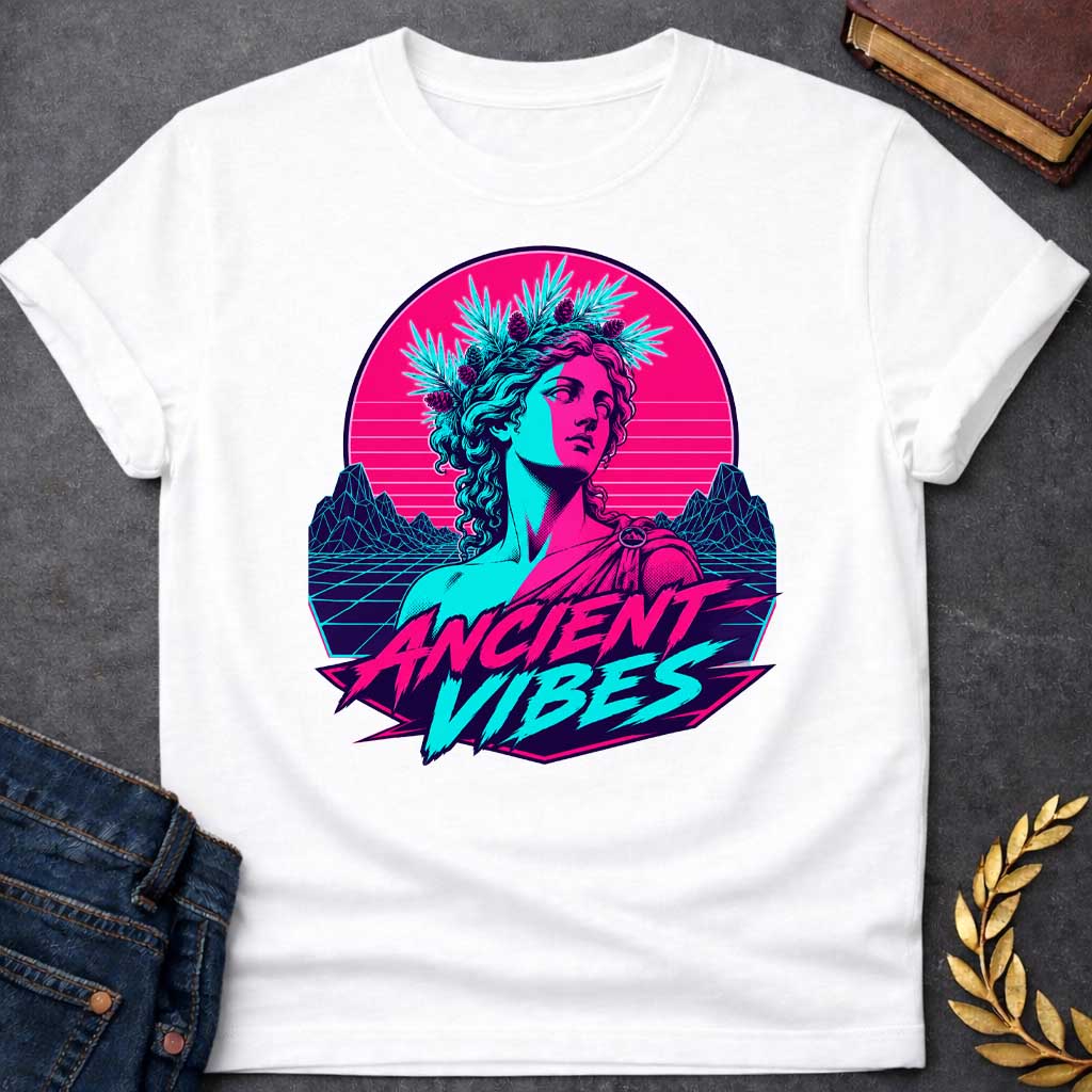 White T-shirt with a Vaporwave-style illustration of a classical Greek Nymph bust in neon magenta and cyan. The figure wears a laurel wreath crown and draped robes with split-color digital aesthetic. Geometric mountains and grid pattern landscape create a retro 80s vibe. Horizontal scan lines suggest digital distortion. Bold text reads 'ANCIENT VIBES' in magenta and cyan with star accents. Navy blue border frames the design. Blends classical Greek aesthetics with modern synthwave style.