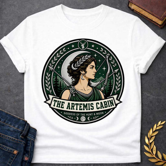 White t-shirt with a Artemis Greek mythology cabin design featuring the goddess of the hunt and moon with a crescent moon, bow and arrows, forest mountains, stars, laurel branches, and deer symbol. Dark green, silver, cream, and black circular camp-style emblem includes the text “The Artemis Cabin” and “Goddess of the Hunt & Moon.”