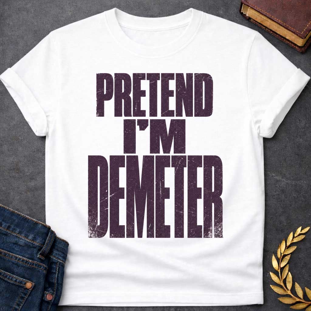 White t-shirt with a Pretend I’m Demeter Greek mythology design featuring bold distressed purple typography on a transparent background. The stacked text reads “PRETEND I’M DEMETER” in a rugged vintage block font, creating a humorous design inspired by Demeter, the Greek goddess of agriculture, harvest, grain, fertility, and the earth.