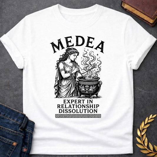White T-shirt with a Classical engraving of Medea, the legendary Greek sorceress, in flowing draped robes with Greek key pattern headband. She stirs a decorative cauldron with magical swirling smoke and stars rising dramatically from within. Black and white line art style with intricate detailing. Text reads 'Medea' above and 'Expert in Relationship Dissolution' below with Greek key border. Dark humor celebrates Medea's infamous reputation for magical vengeance and relationship destruction.
