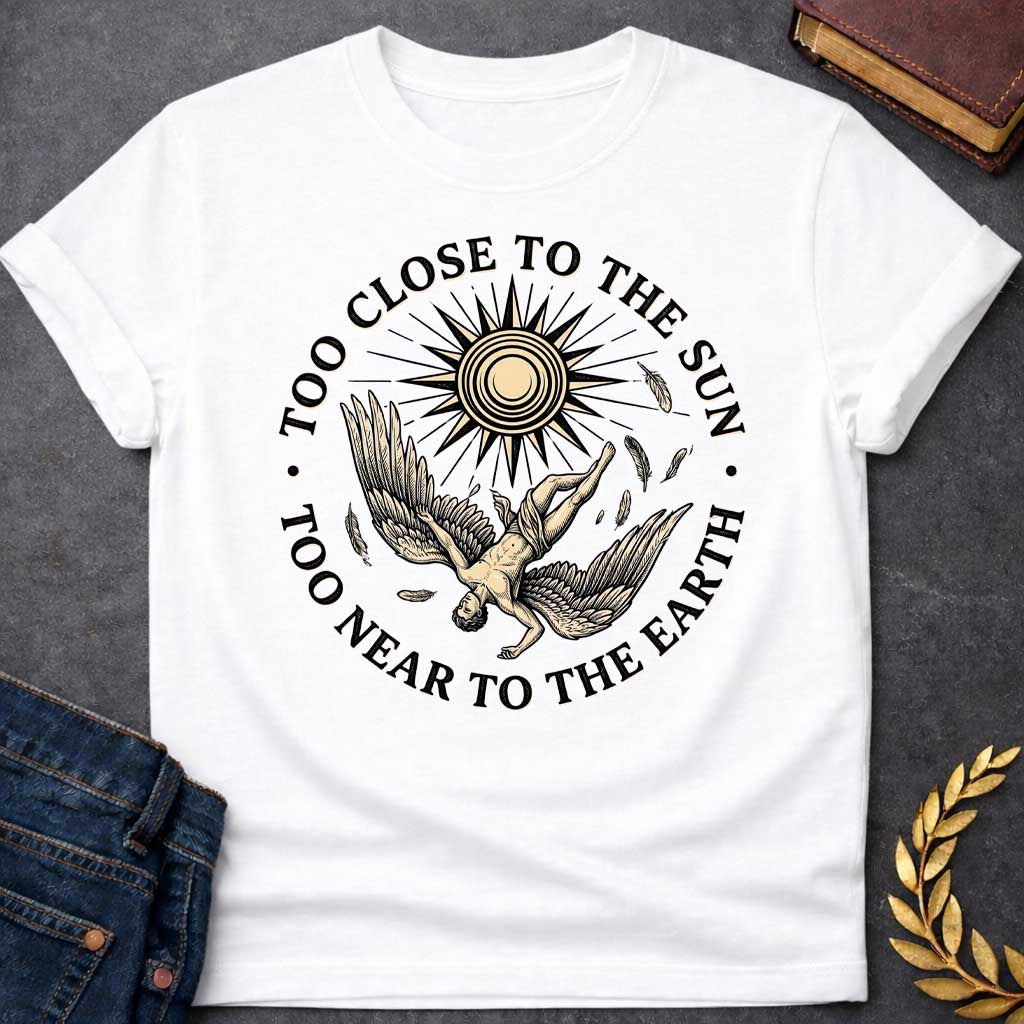 White t-shirt with a vintage engraved-style illustration. A winged figure of Icarus plummets downward upside down as loose feathers drift through the air beneath a large, radiating sun emblem. Encircling the detailed central artwork, bold black serif text reads "TOO CLOSE TO THE SUN" along the top arch and "TOO NEAR TO THE EARTH" along the bottom curve.
