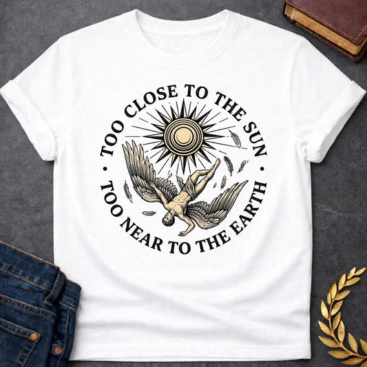 White t-shirt with a vintage engraved-style illustration. A winged figure of Icarus plummets downward upside down as loose feathers drift through the air beneath a large, radiating sun emblem. Encircling the detailed central artwork, bold black serif text reads "TOO CLOSE TO THE SUN" along the top arch and "TOO NEAR TO THE EARTH" along the bottom curve.