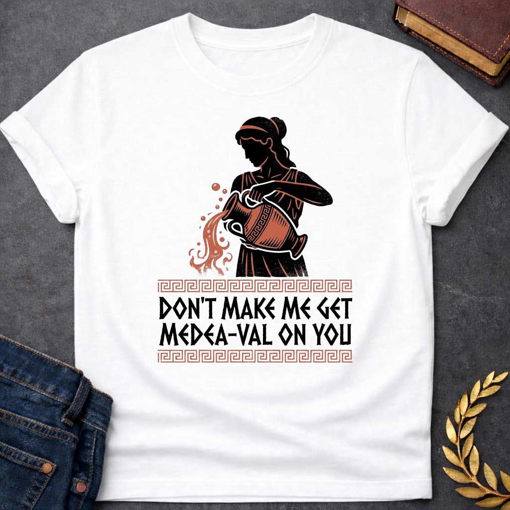 White T-shirt with A Silhouetted figure of Medea, legendary Greek sorceress, rendered in black and rust-red. She wears classical robes and headband while holding an ornate cauldron with magical flames and sparks bursting forth. Greek key pattern borders frame the design. Text reads 'Don't Make Me Get Medea-Val On You' - wordplay combining her name with modern slang. Celebrates Medea's fearsome magical and destructive powers with contemporary humor.