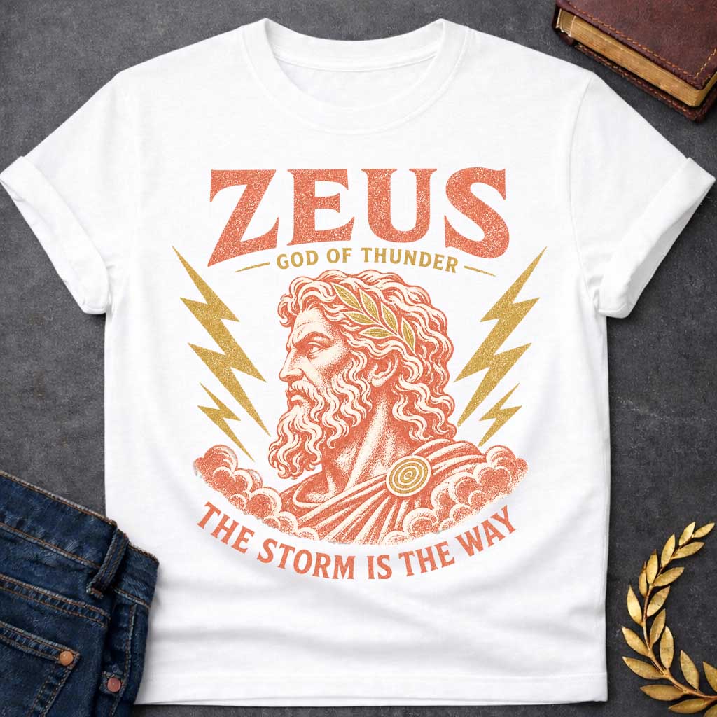 White t-shirt with a Vintage Zeus Greek mythology design featuring the bearded god of thunder wearing a golden laurel crown, surrounded by lightning bolts and storm clouds. Distressed terracotta and gold artwork includes the text “Zeus,” “God of Thunder,” and “The Storm Is the Way,” 