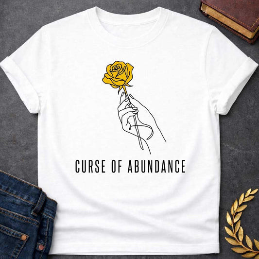 White t-shirt with A Minimalist Greek mythology design featuring a continuous line-art hand delicately holding a golden rose, symbolizing King Midas' legendary golden touch. Below the illustration, the phrase "Curse of Abundance" appears in clean, modern typography. A simple black-and-gold aesthetic creates an elegant, understated design inspired by the tragic Midas myth.