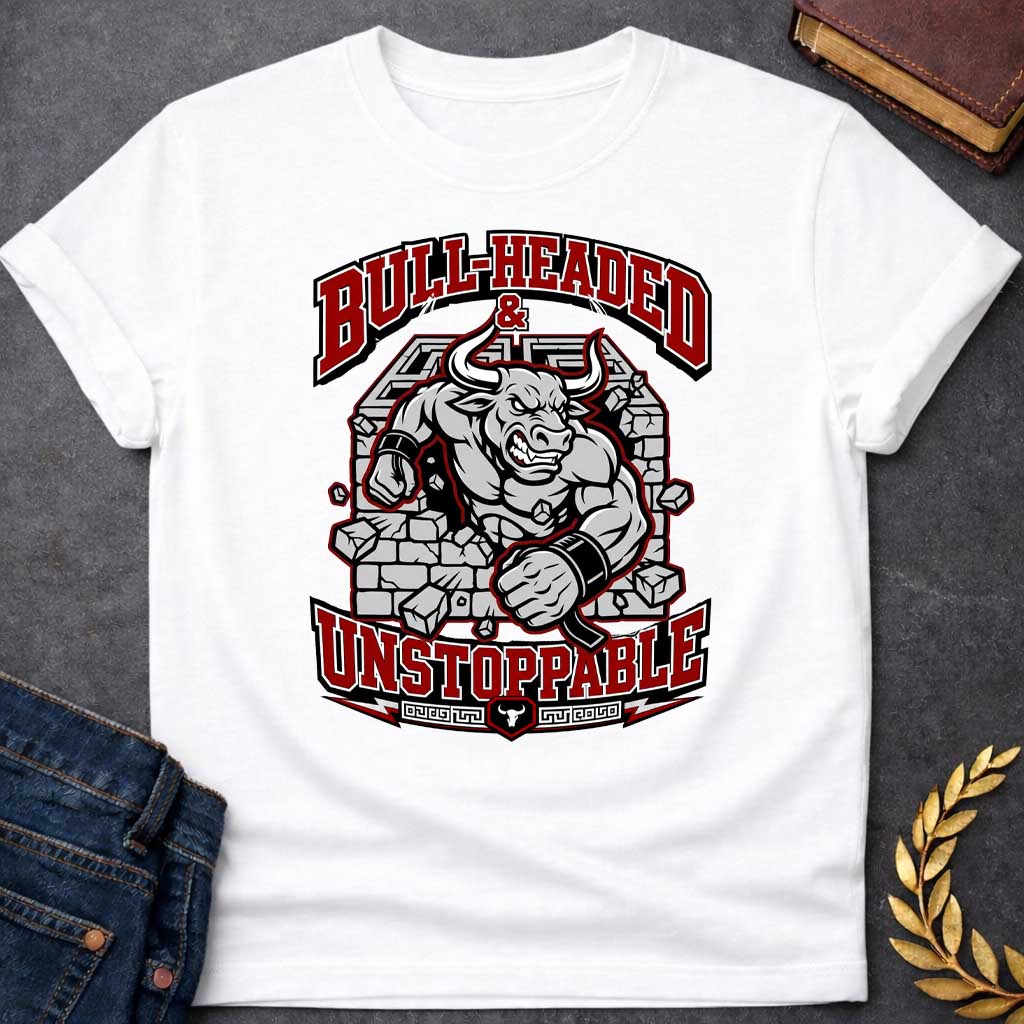 White T-shirt with a High-impact sports design featuring a muscular Minotaur bursting through a crumbling stone wall in red, gray, and white. The aggressive bull-headed figure displays defined musculature and determination. Text reads 'Bull-Headed & Unstoppable' in bold red and black lettering. Greek key pattern and bull symbol anchor the bottom. Combines Greek mythology with modern gym and sports culture, celebrating stubborn strength and unstoppable power.