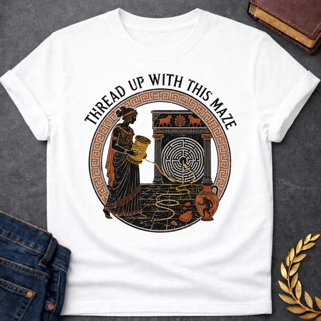 White T-shirt with A distressed, ancient Greek pottery-style t-shirt graphic. Inside a circular terracotta Greek key frame, a black figure of Ariadne holds a large spool, unwinding a golden thread that leads into a circular maze on a stone structure. An amphora vase with a Minotaur stands nearby. Arched above the scene, black text reads "THREAD UP WITH THIS MAZE" in a rustic serif font.